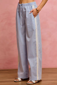Person wearing blue checkered pants with a white stripe on a pink background