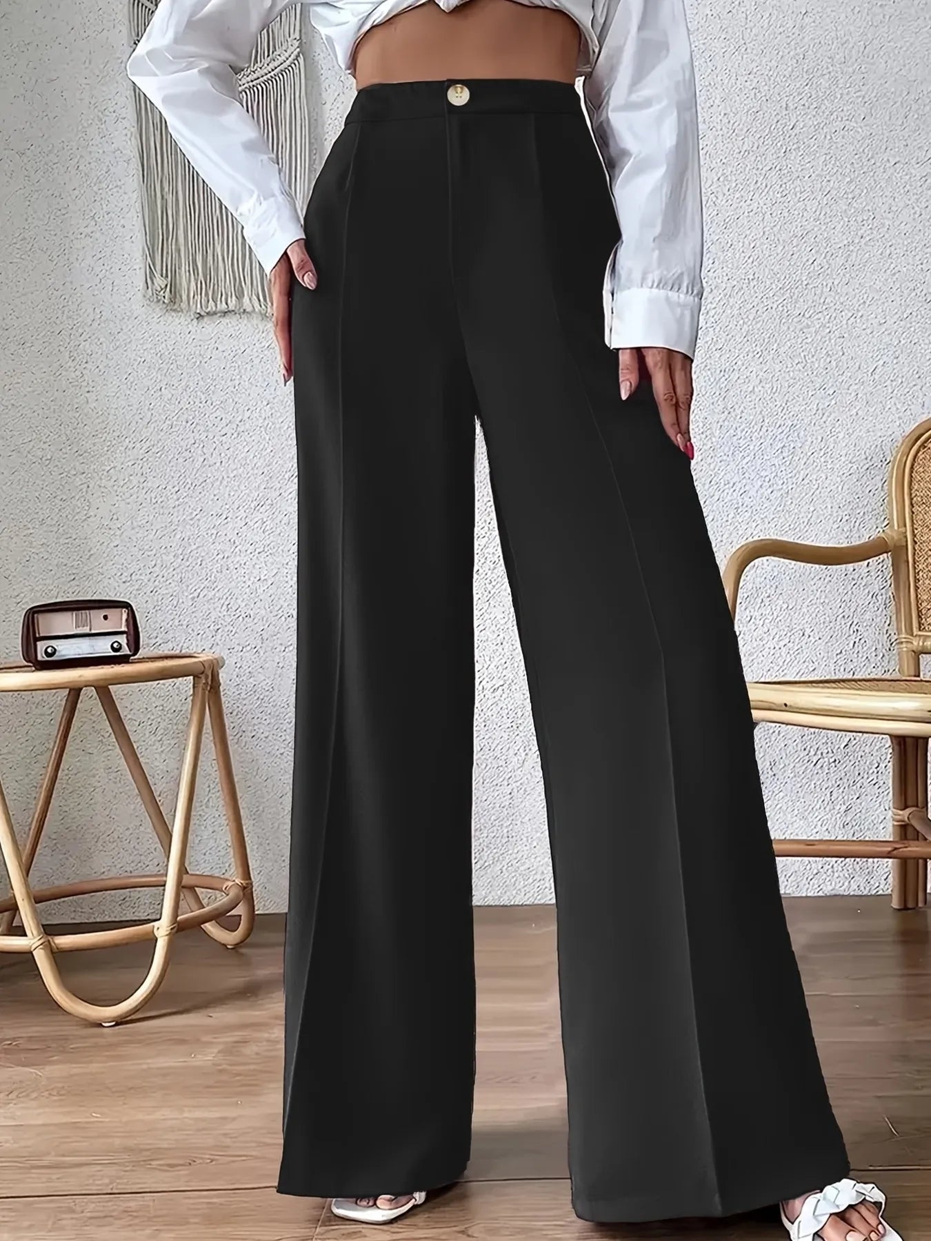 Person wearing black wide-leg pants and a white shirt in a room with a textured wall and wooden floor.