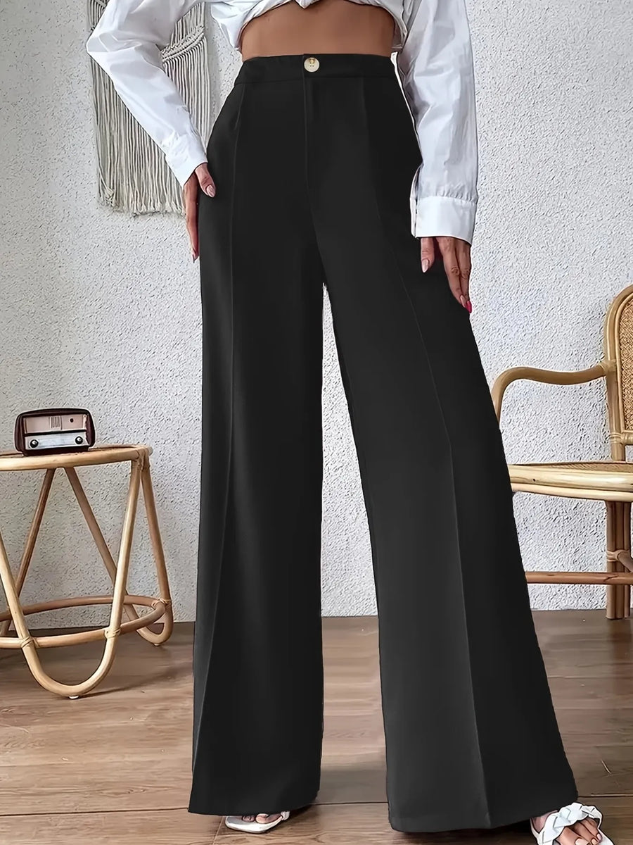 Person wearing black wide-leg pants and a white shirt in a room with a textured wall and wooden floor.