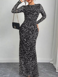 Woman wearing a gray leopard print dress with a black handbag against a white wall.
