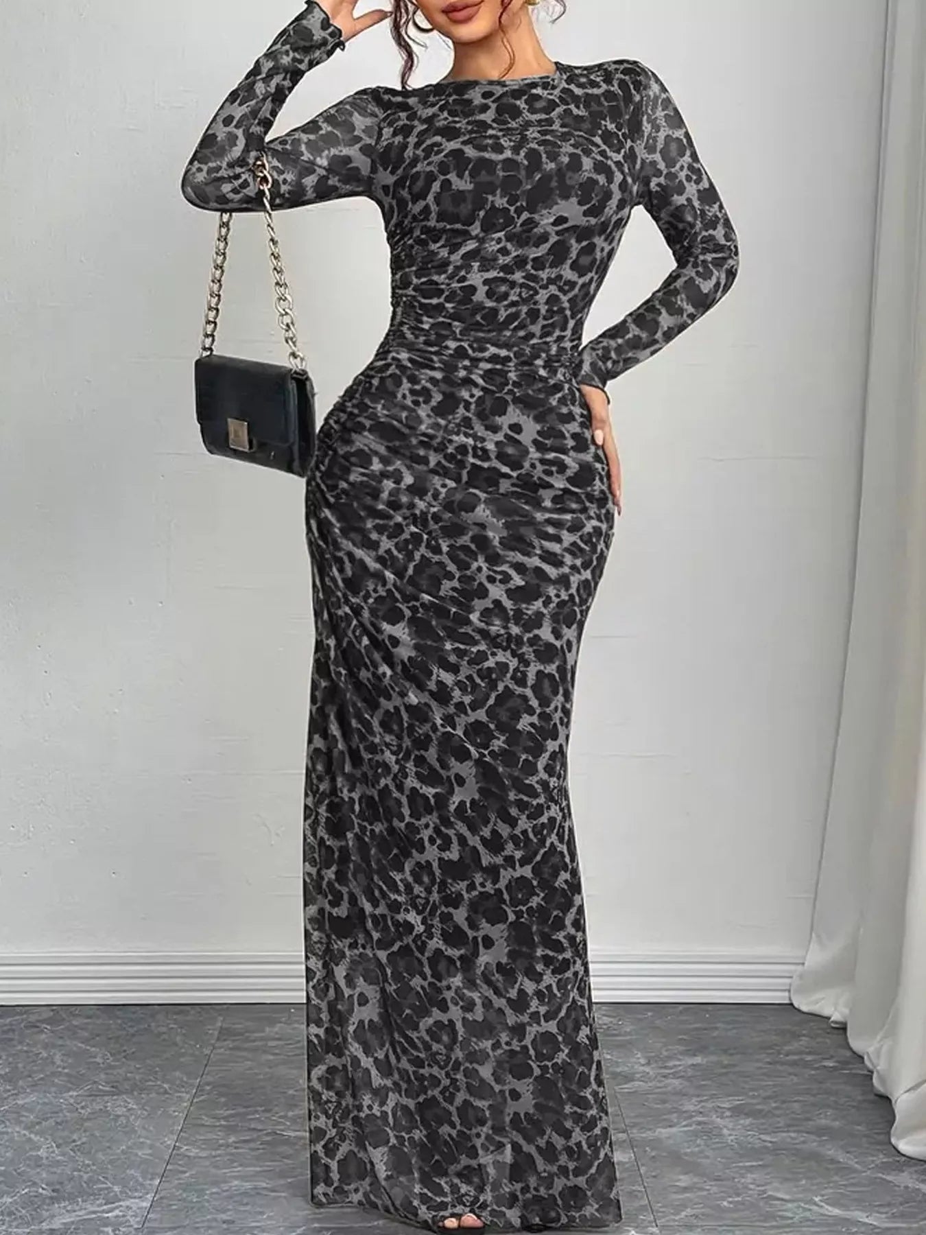 Woman wearing a gray leopard print dress with a black handbag against a white wall.