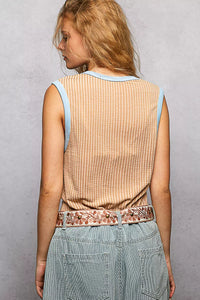 Person wearing a beige sleeveless top with a patterned belt and light blue jeans on a gray background