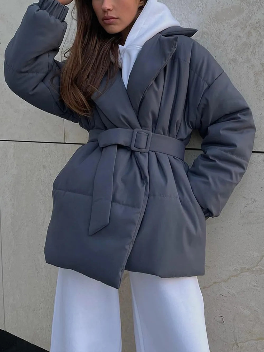 Person wearing a gray puffer coat with a belt against a neutral wall.