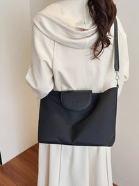 Person wearing a black shoulder bag with a visible brand logo against a neutral background