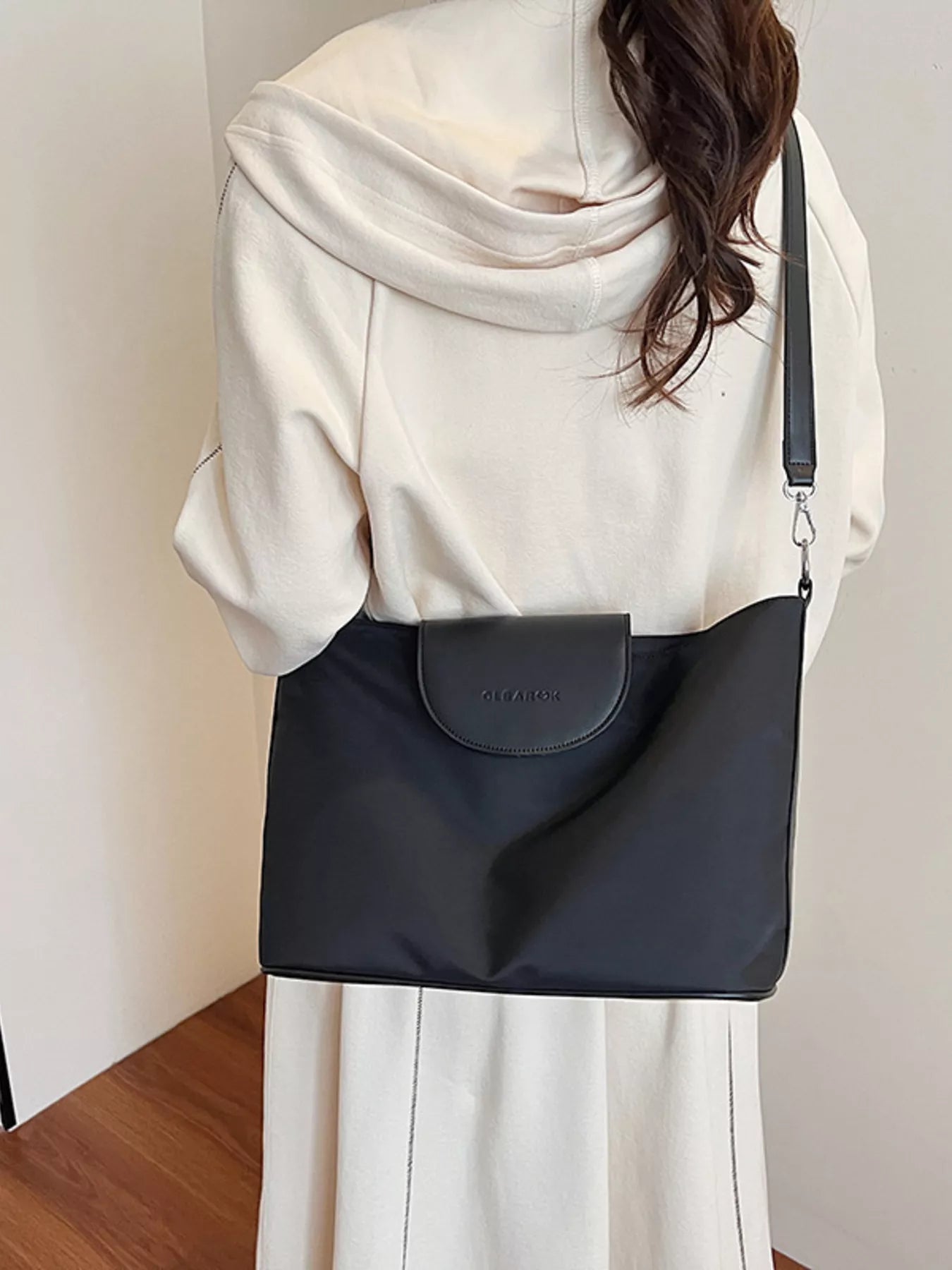 Person wearing a black shoulder bag with a visible brand logo against a neutral background