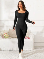 Woman wearing a black bodysuit in a white room with flowers on a table.