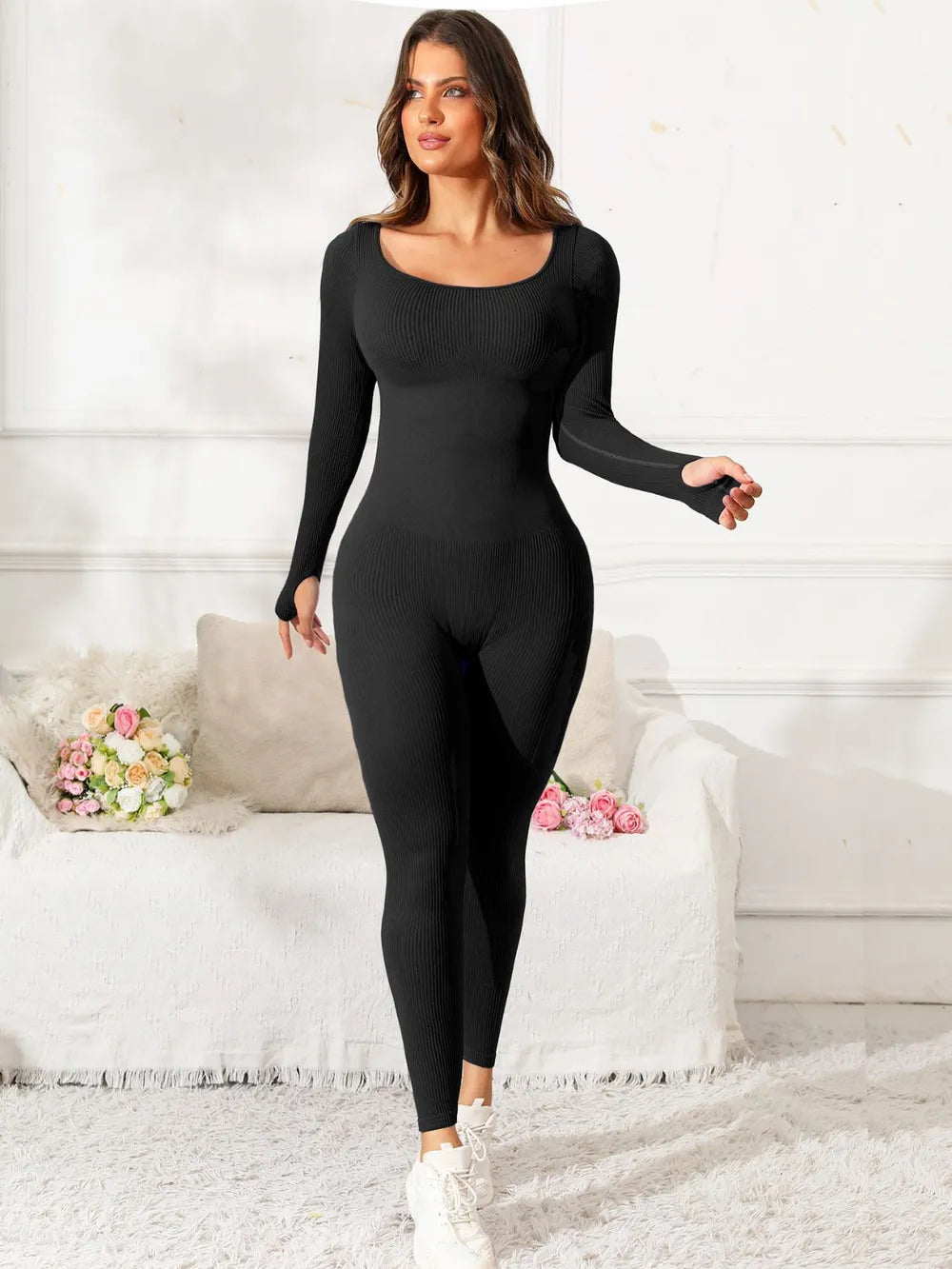 Woman wearing a black bodysuit in a white room with flowers on a table.
