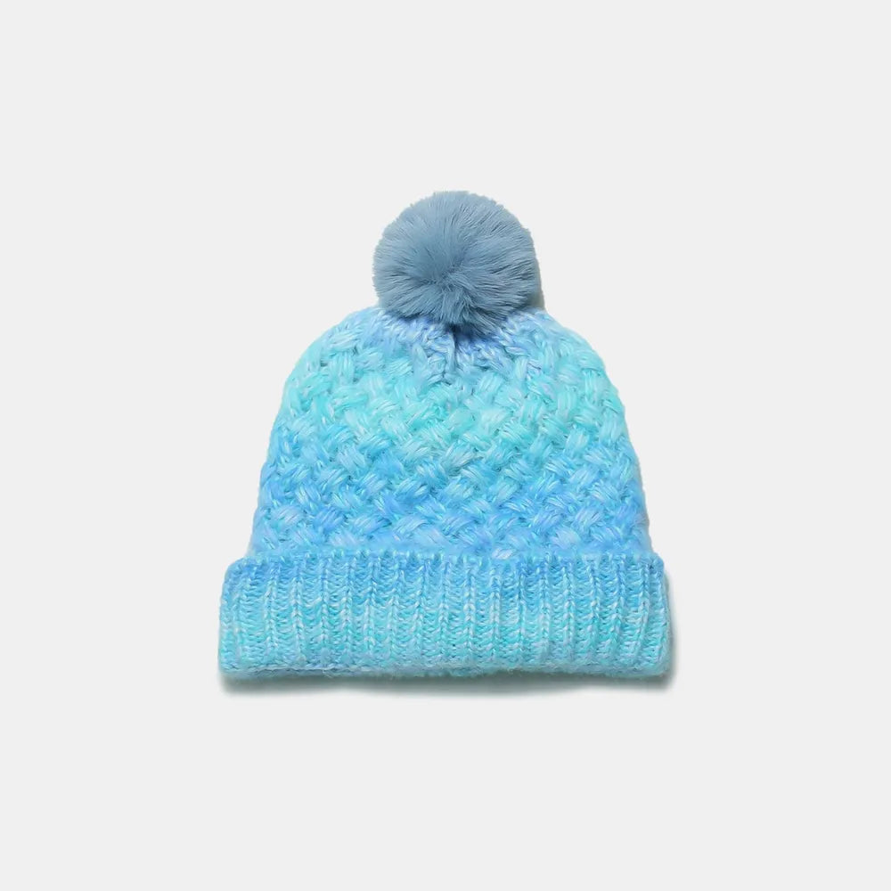 Blue knitted beanie with a pom-pom on a light gray background