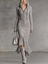 Woman wearing a gray ribbed dress with lace hem and white boots, holding a silver handbag against a plain background.