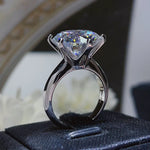 Silver ring with a large diamond on a black cushion with a blurred floral background