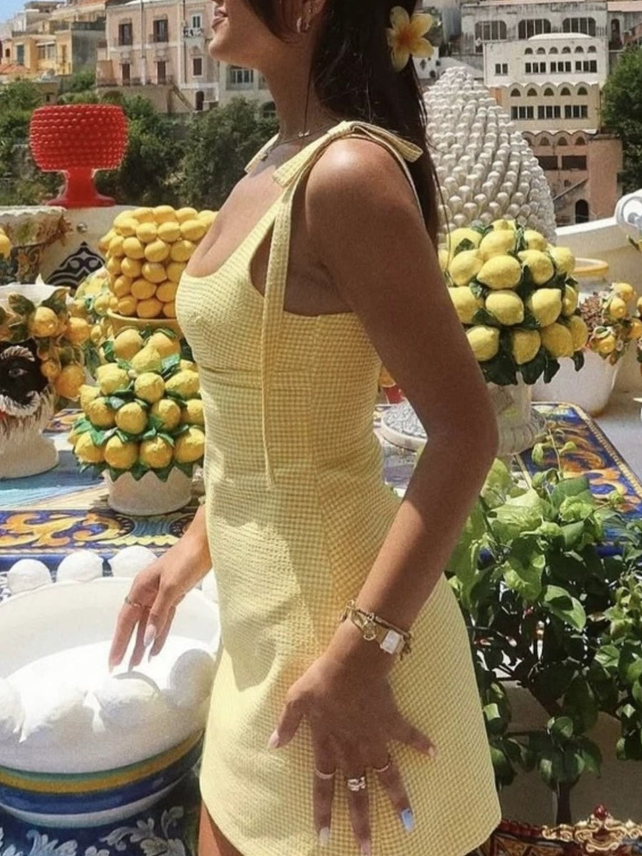 Woman in a yellow dress standing in front of lemon decorations and buildings.