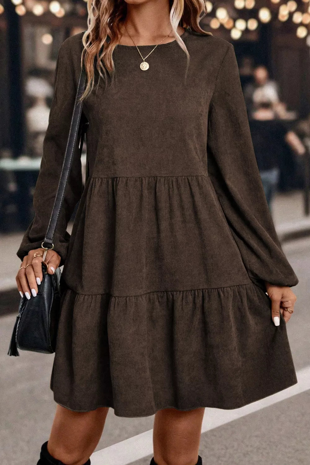 Woman wearing a brown dress with long sleeves and layered skirt, holding a black handbag.