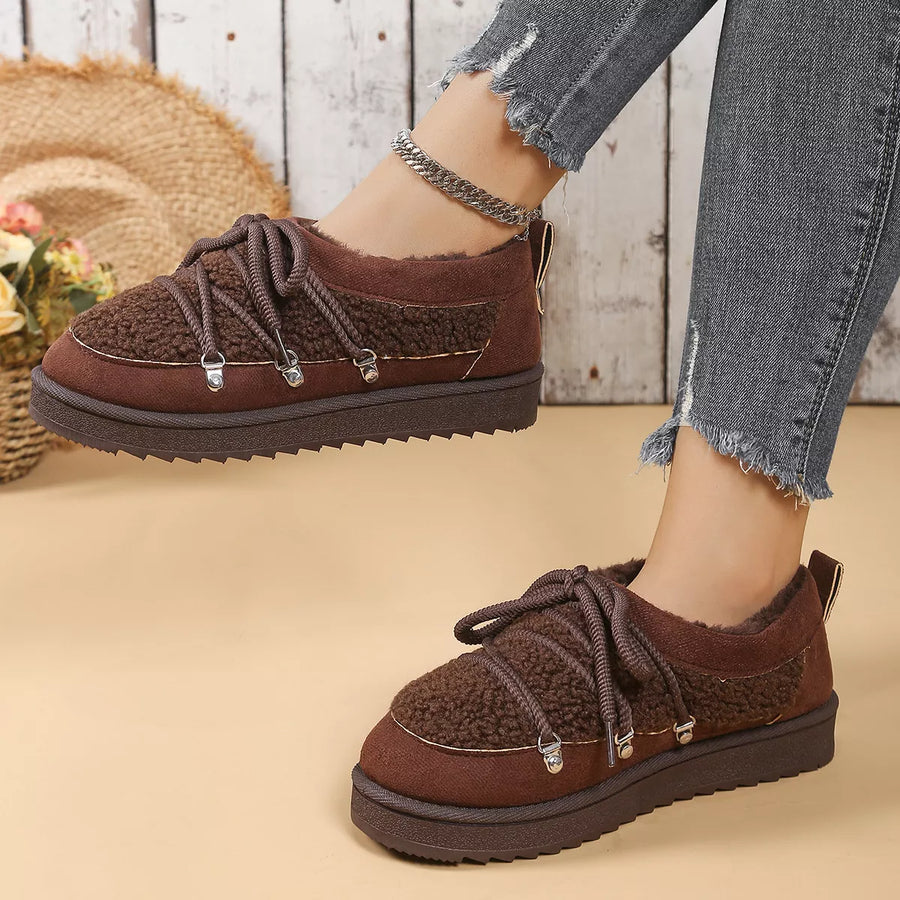 Brown textured shoes worn with denim jeans on a beige surface.