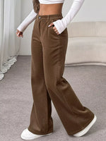 Person wearing brown wide-leg pants with a white top and shoes in a neutral setting