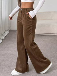Person wearing brown wide-leg pants with a white top and shoes in a neutral setting