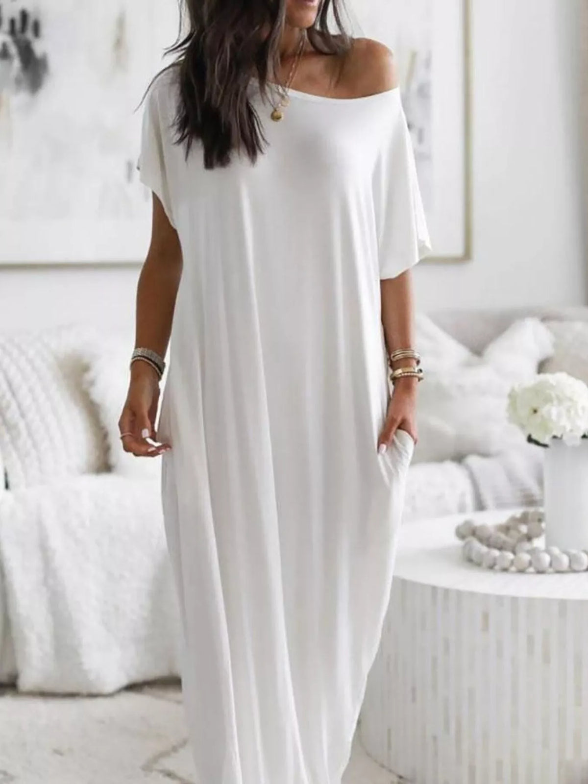 Woman wearing a white off-shoulder dress in a minimalistic room.