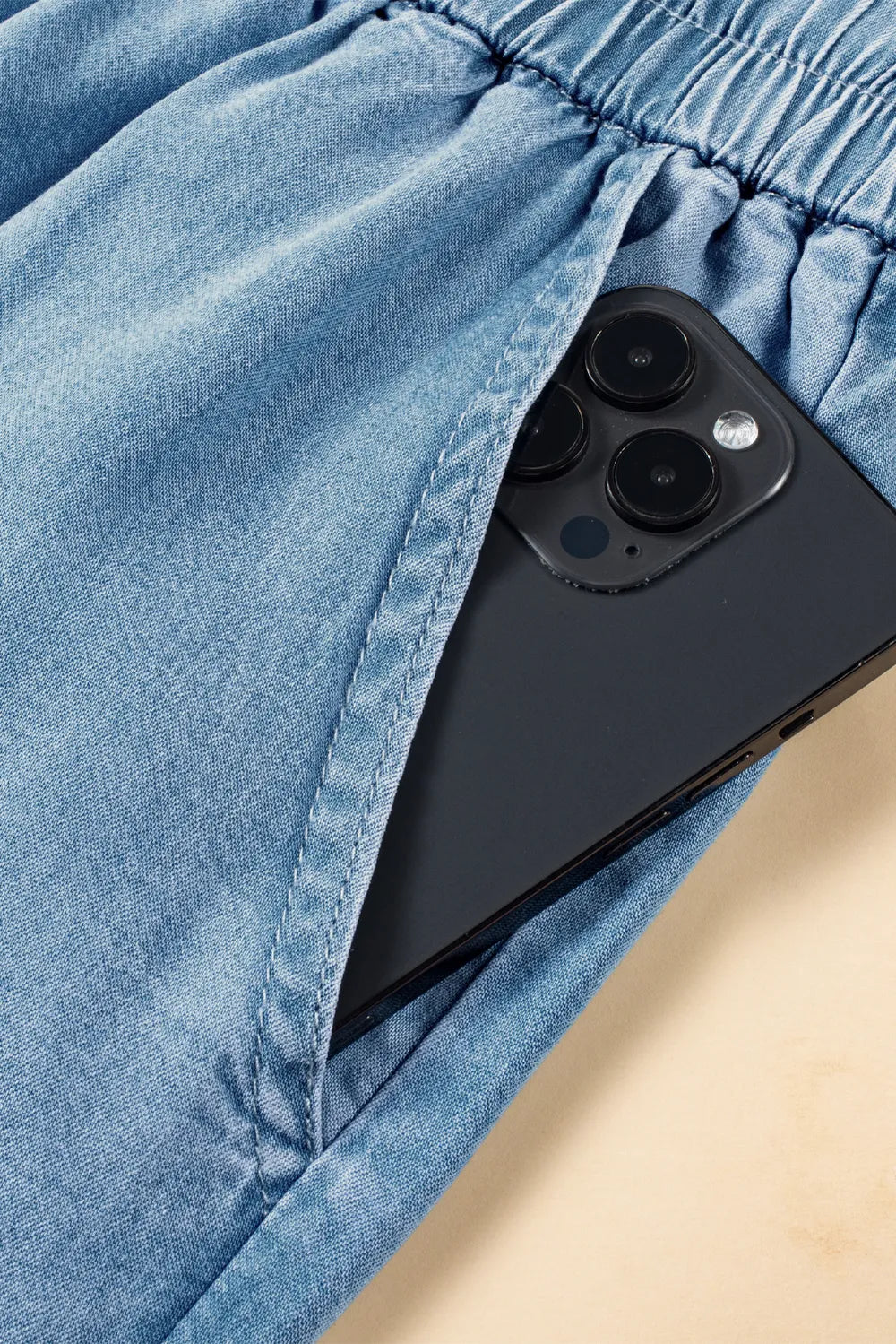 Black smartphone peeking out from a blue denim pocket on a wooden surface