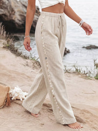 Person wearing beige pants with button details on a beach.
