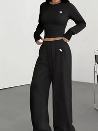 Person wearing a black cropped sweatshirt and wide-leg pants with a brand logo on a plain background