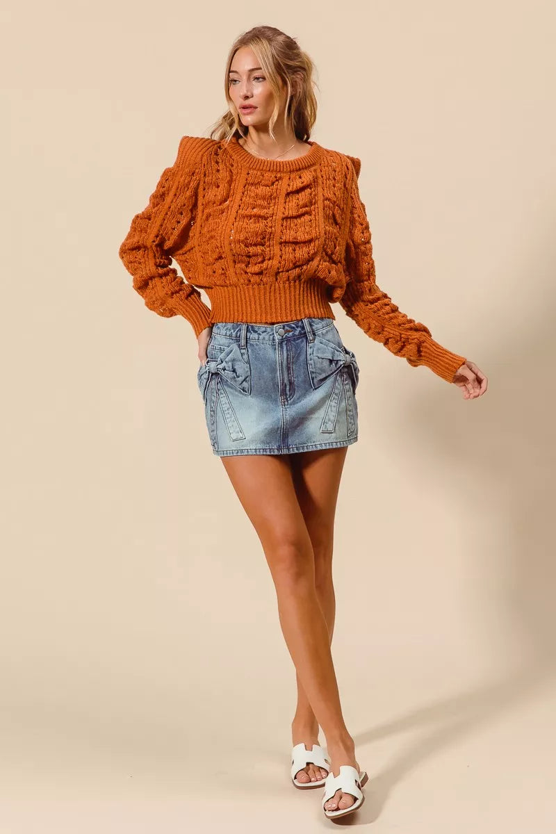 Woman wearing an orange cable knit sweater and denim skirt on a beige background