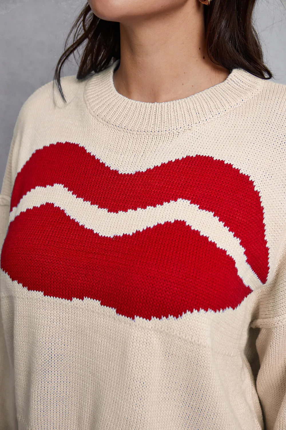Beige sweater with a large red and white abstract design on a neutral background