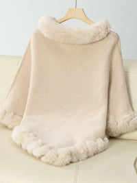 Beige poncho with fur trim draped over a couch against a white background