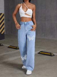 Person wearing a white crop top and light blue jeans with butterfly designs in an industrial setting.