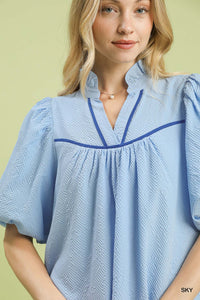 Woman wearing a light blue blouse with blue trim on a yellow background