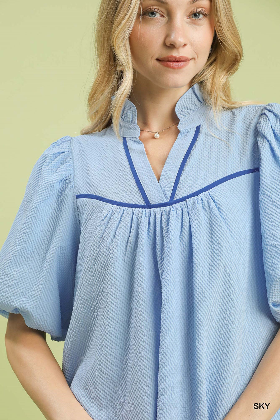 Woman wearing a light blue blouse with blue trim on a yellow background
