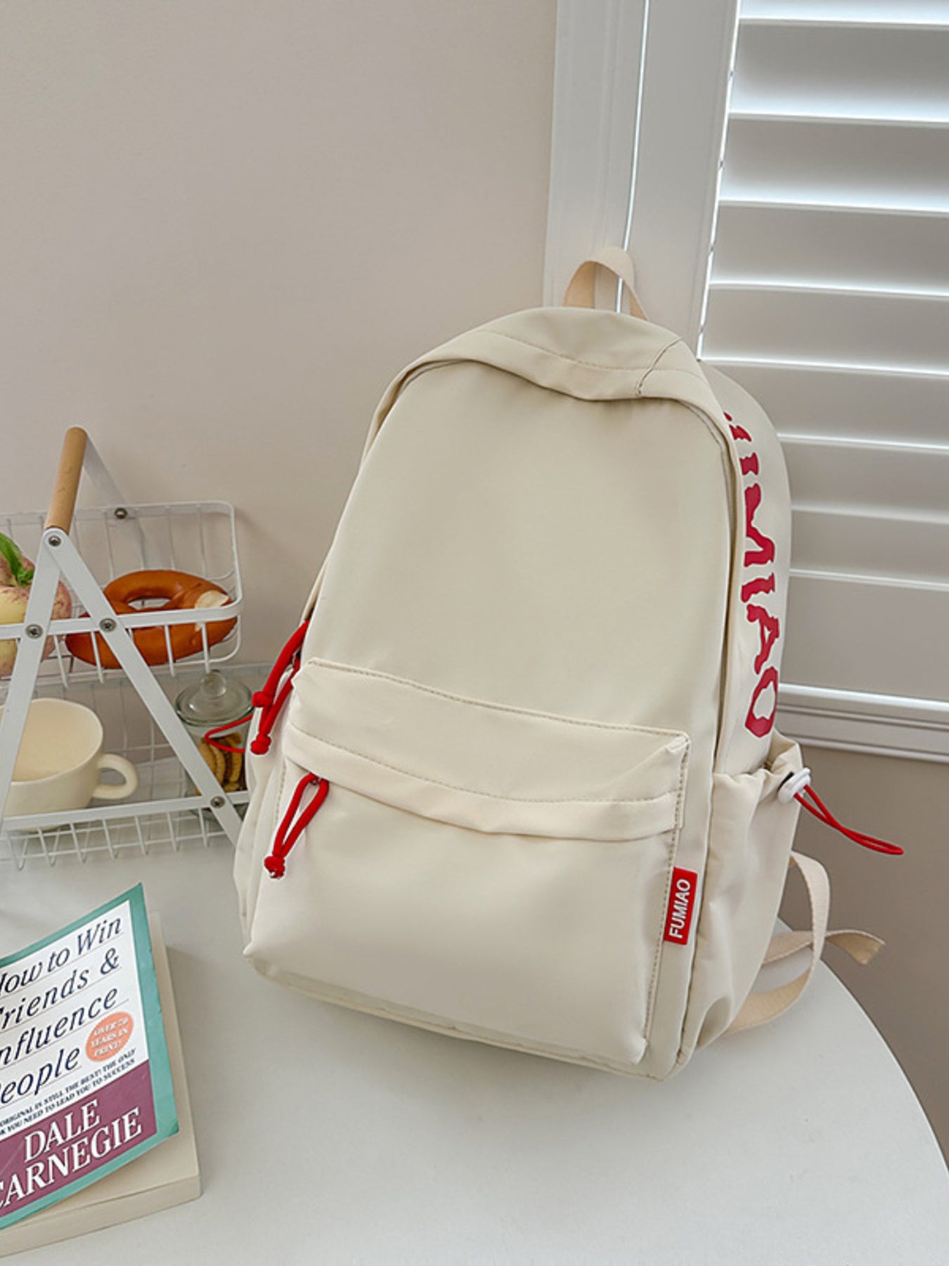 Beige backpack with red lettering on a white surface next to a book