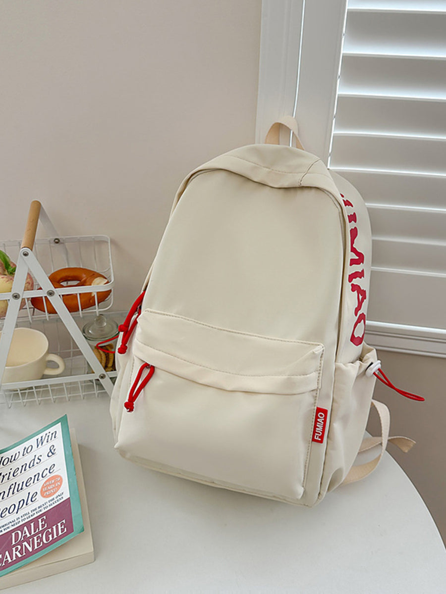 Beige backpack with red lettering on a white surface next to a book