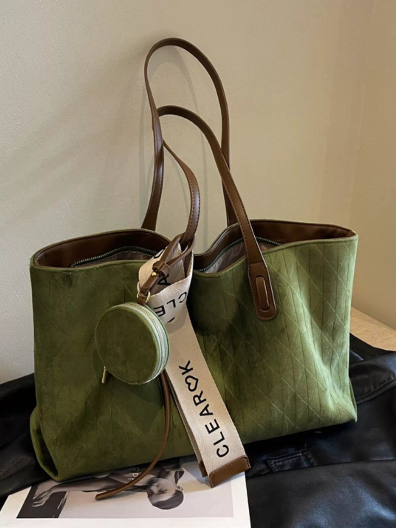 Green tote bag with brown handles on a white surface