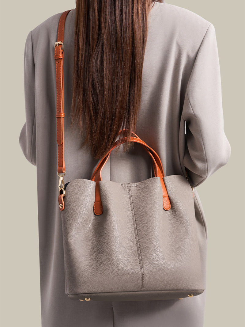 Person wearing a gray tote bag with orange handles and strap on a neutral background