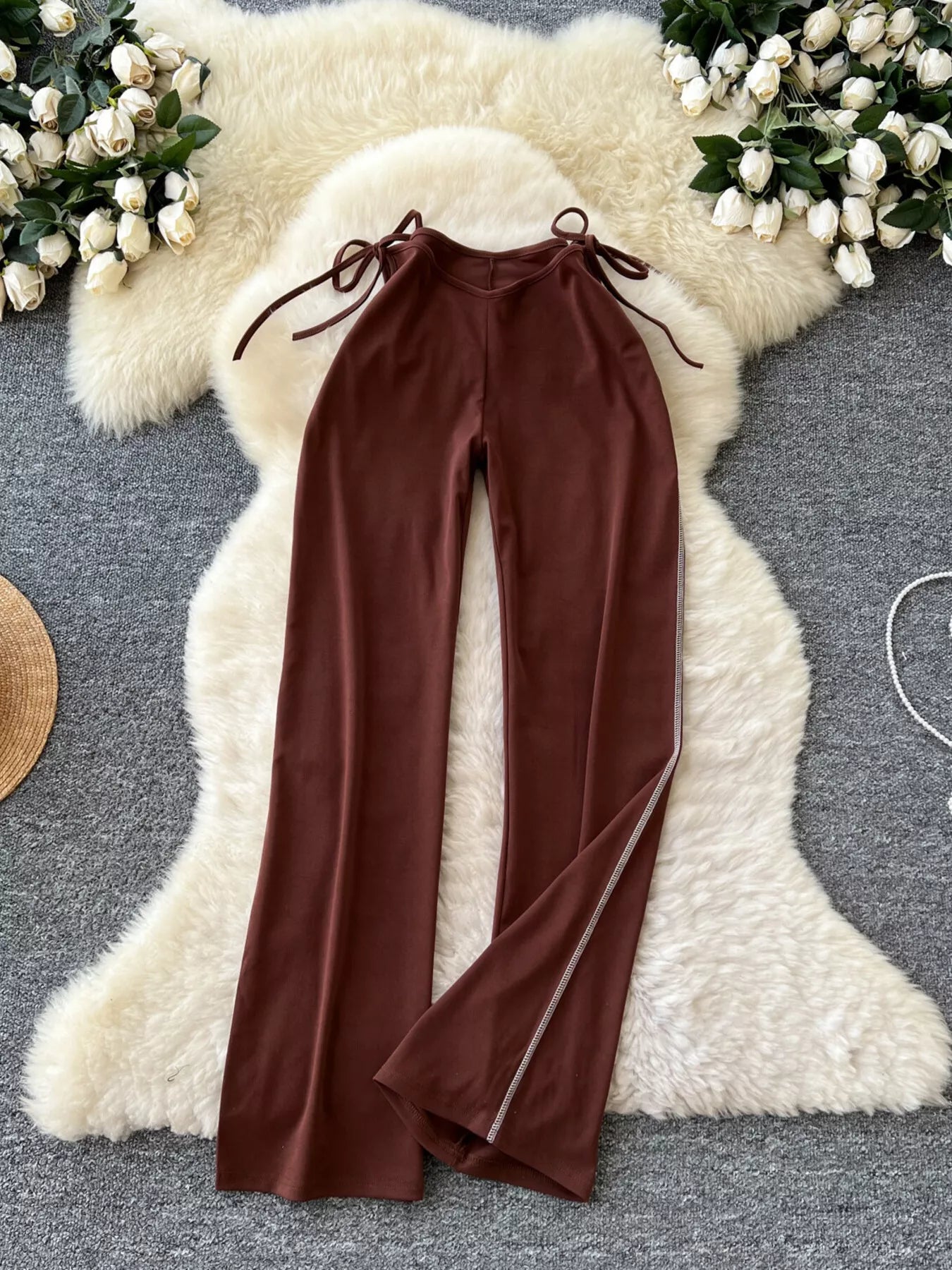 Brown pants on a hanger against a textured white surface with floral decorations.