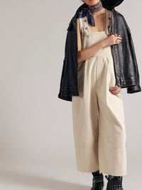 Person wearing a black jacket, beige overalls, and black boots on a plain background