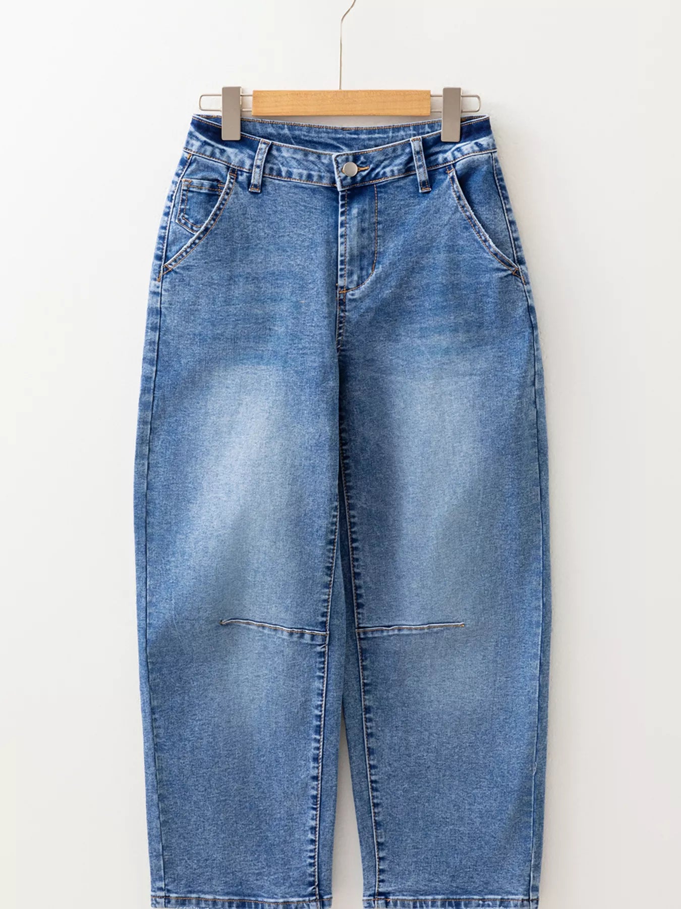 Blue jeans hanging on a wooden hanger against a white background