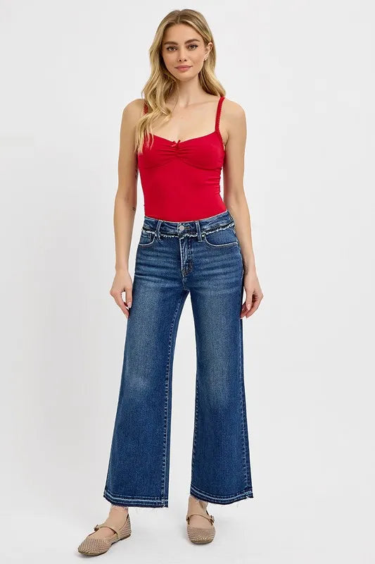 Woman wearing a red tank top and blue jeans on a white background