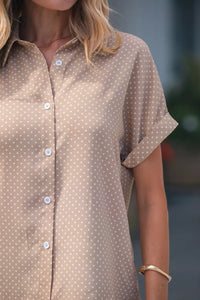 Close-up of a person wearing a brown polka dot shirt with a blurred background