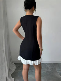 Person wearing a black dress with a white ruffled hem against a plain background