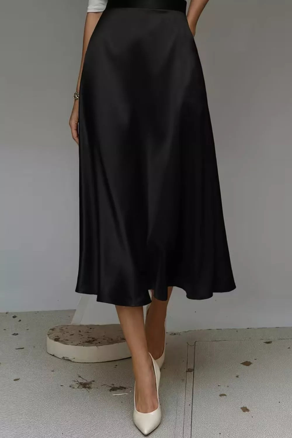 Person wearing a black satin skirt with white shoes on a plain background