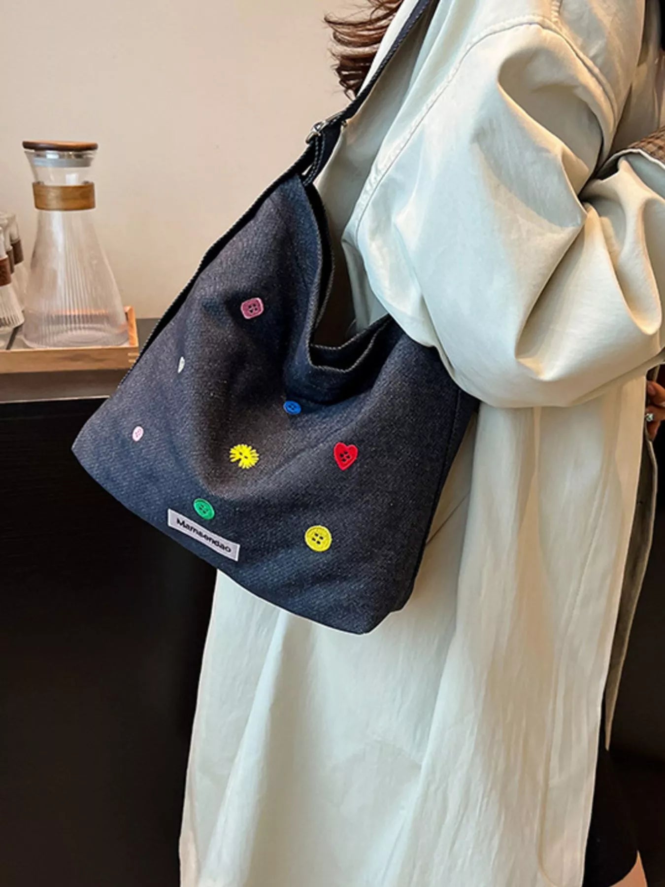 Black bag with colorful heart and smiley face patterns hanging on a person wearing a light-colored coat.