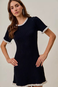 Woman wearing a black dress with white trim on a plain background
