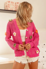 Person wearing a pink knitted cardigan with floral embellishments indoors.