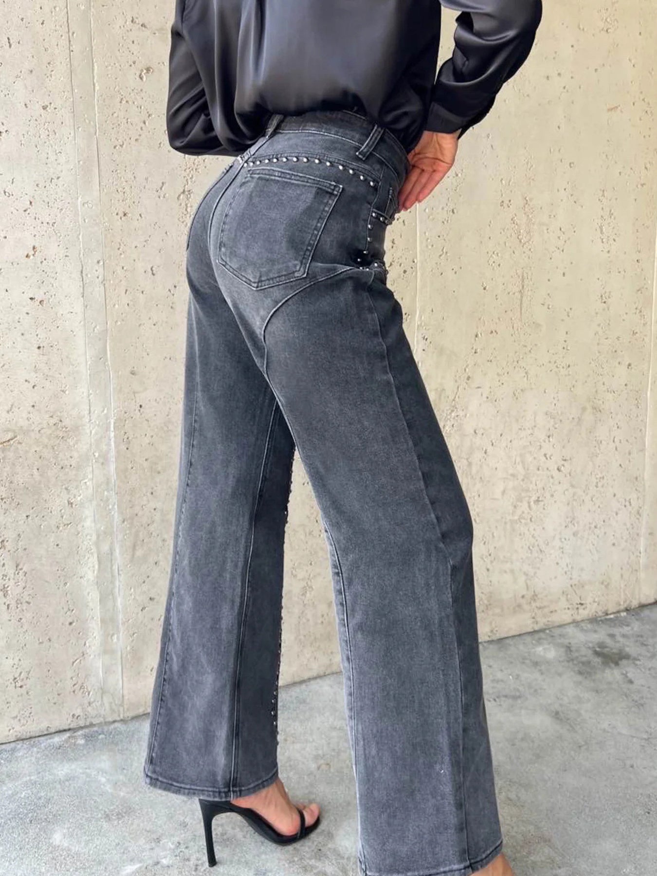Person wearing black studded jeans against a beige wall.