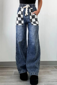 Person wearing blue jeans with a checkered top in a minimal indoor setting