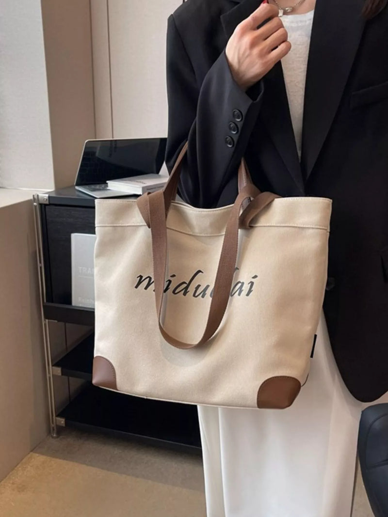 Person holding a beige tote bag with 'midulai' branding in an indoor setting.