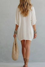 Woman wearing a white dress holding a woven bag against a plain background
