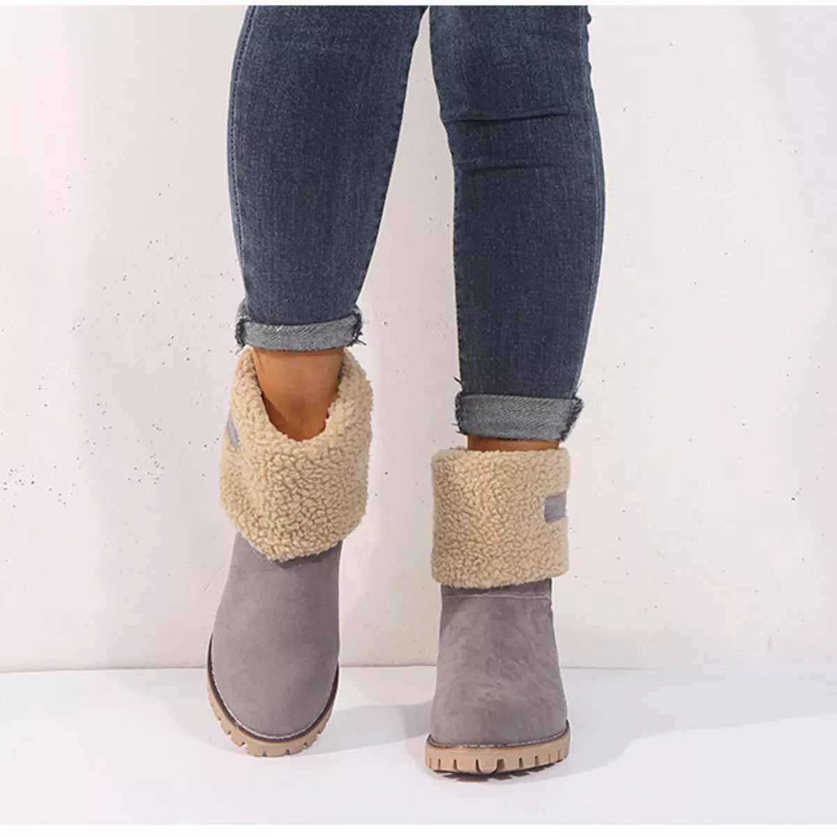 Gray suede boots with beige shearling cuffs worn with rolled-up jeans on a white background