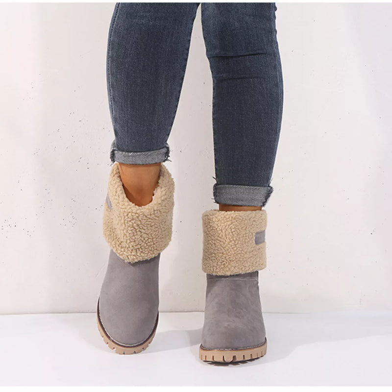 Gray suede boots with beige shearling cuffs worn with rolled-up jeans on a white background