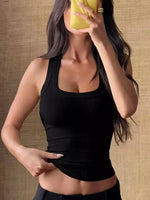 Woman wearing a black tank top against a textured wall.